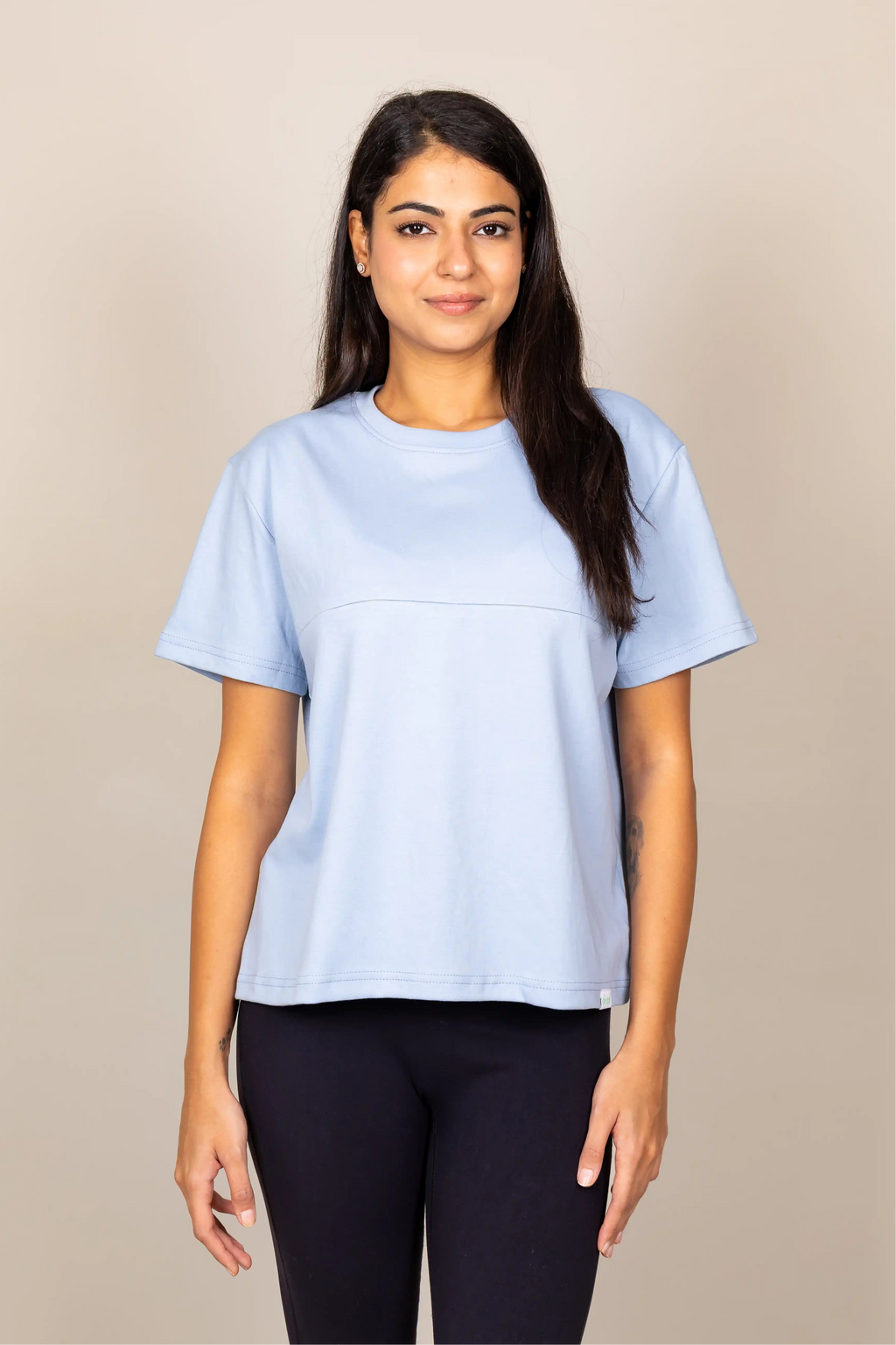 A woman modeling a light blue short-sleeve crewneck t-shirt against a plain beige studio background.