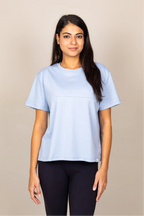 A woman modeling a light blue short-sleeve crewneck t-shirt against a plain beige studio background.