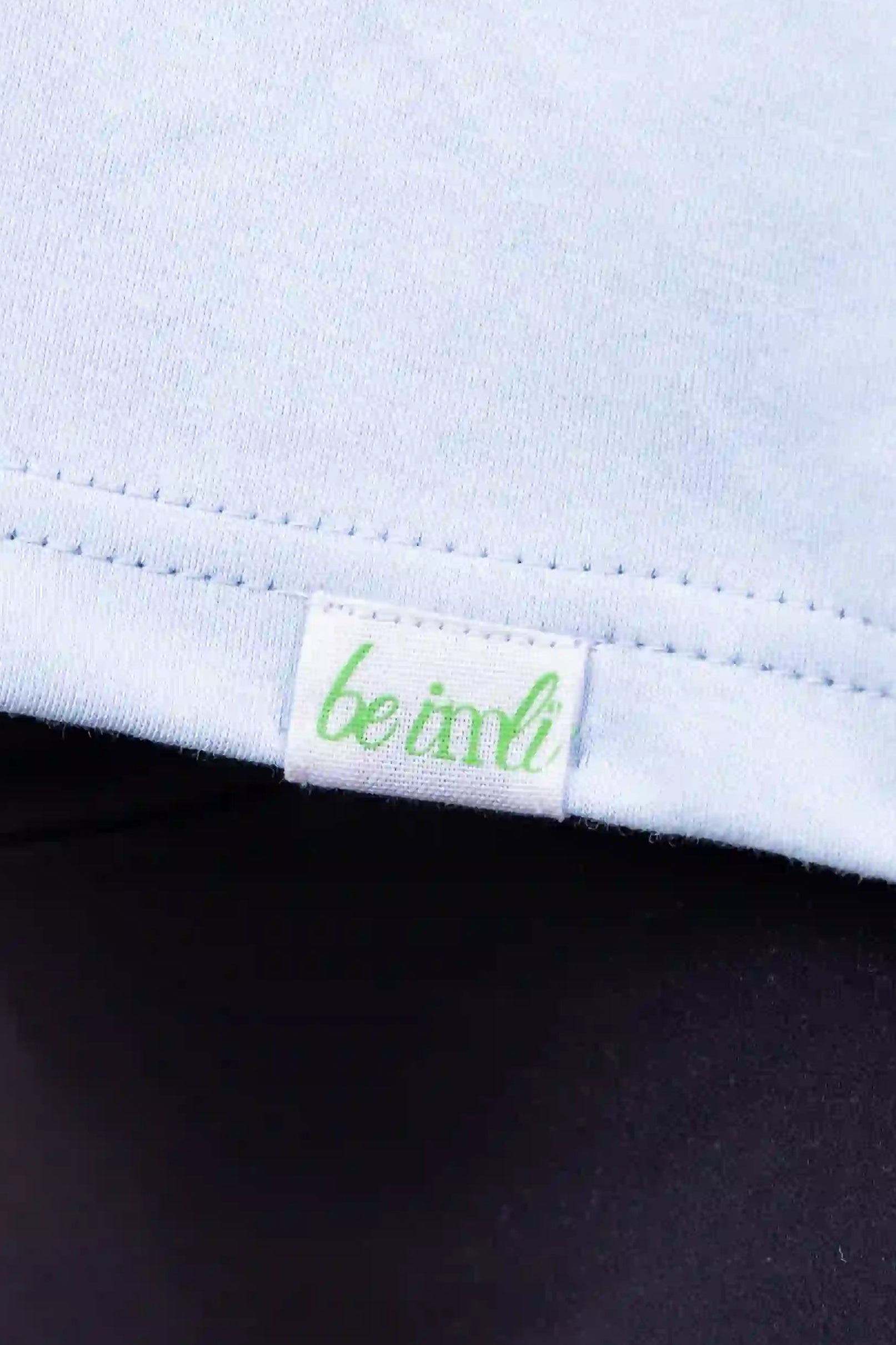 Close-up of a light blue top with a small green and white 'be imli' brand tag near the hem, worn with dark leggings.